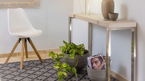 Una habitación moderna con una silla blanca, una mesa con lámpara, un cuadro abstracto enmarcado y una planta en maceta.