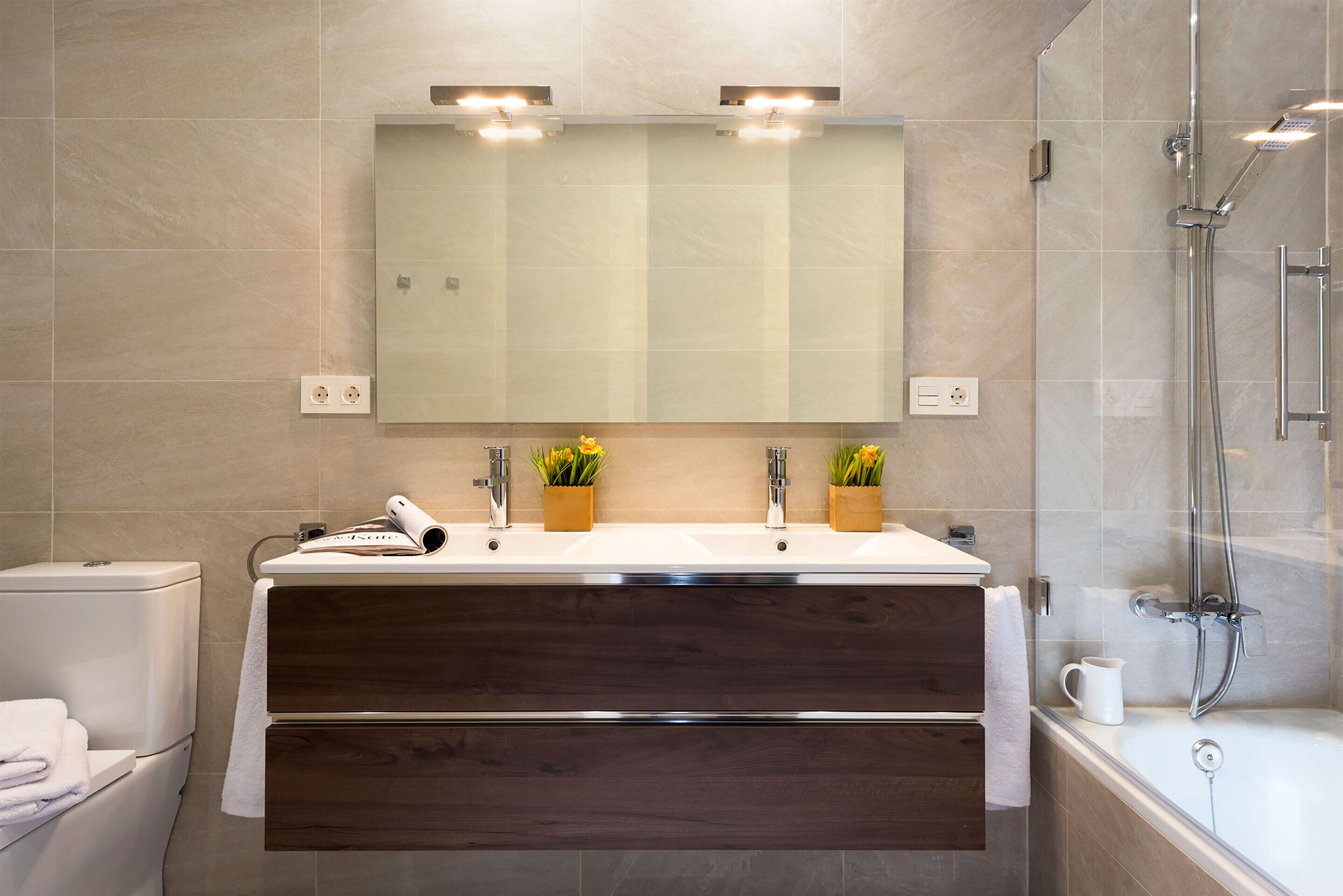 A modern bathroom with a double sink vanity, a toilet, a shower, and a large mirror.