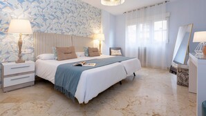 Un dormitorio con una cama grande, dos mesitas de noche, un tocador, un espejo y una ventana con cortinas.