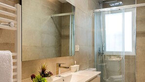Un baño moderno con un espejo grande, cabina de ducha de vidrio y lavamanos blanco.