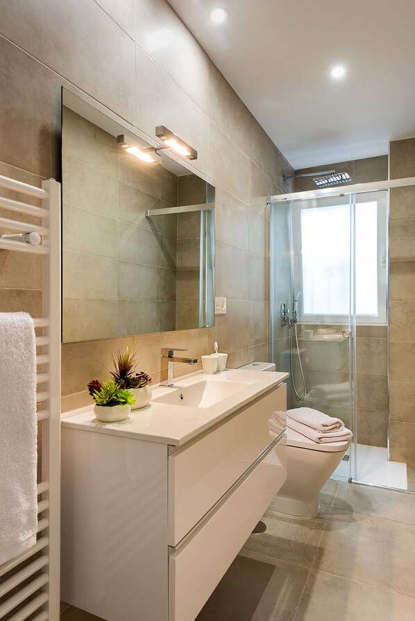 Un baño moderno con un espejo grande, cabina de ducha de vidrio y lavamanos blanco.