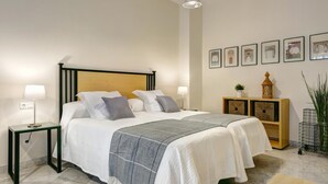 A neatly arranged bedroom with a bed, bedside lamps, a nightstand, a bedside table, a wooden nightstand, a wall-mounted shelf, and framed pictures. - Genteel Home Tomás de Ibarra (Seville)