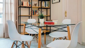 A dining area with a glass table, white chairs, a bookshelf with books and decorative items, and a door with a brass handle. - Genteel Home Tomás de Ibarra (Seville)