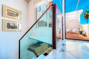 Ein modernes Interieur mit einer Glastreppe, gerahmten Bildern an der Wand und Blick auf die Außenterrasse mit Liegestühlen.