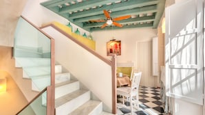 Eine Treppe mit Glasgeländern führt zu einem Essbereich mit Schachbrettboden und Deckenventilator.