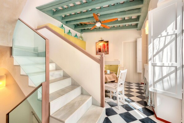 Eine Treppe mit Glasgeländern führt zu einem Essbereich mit Schachbrettboden und Deckenventilator.