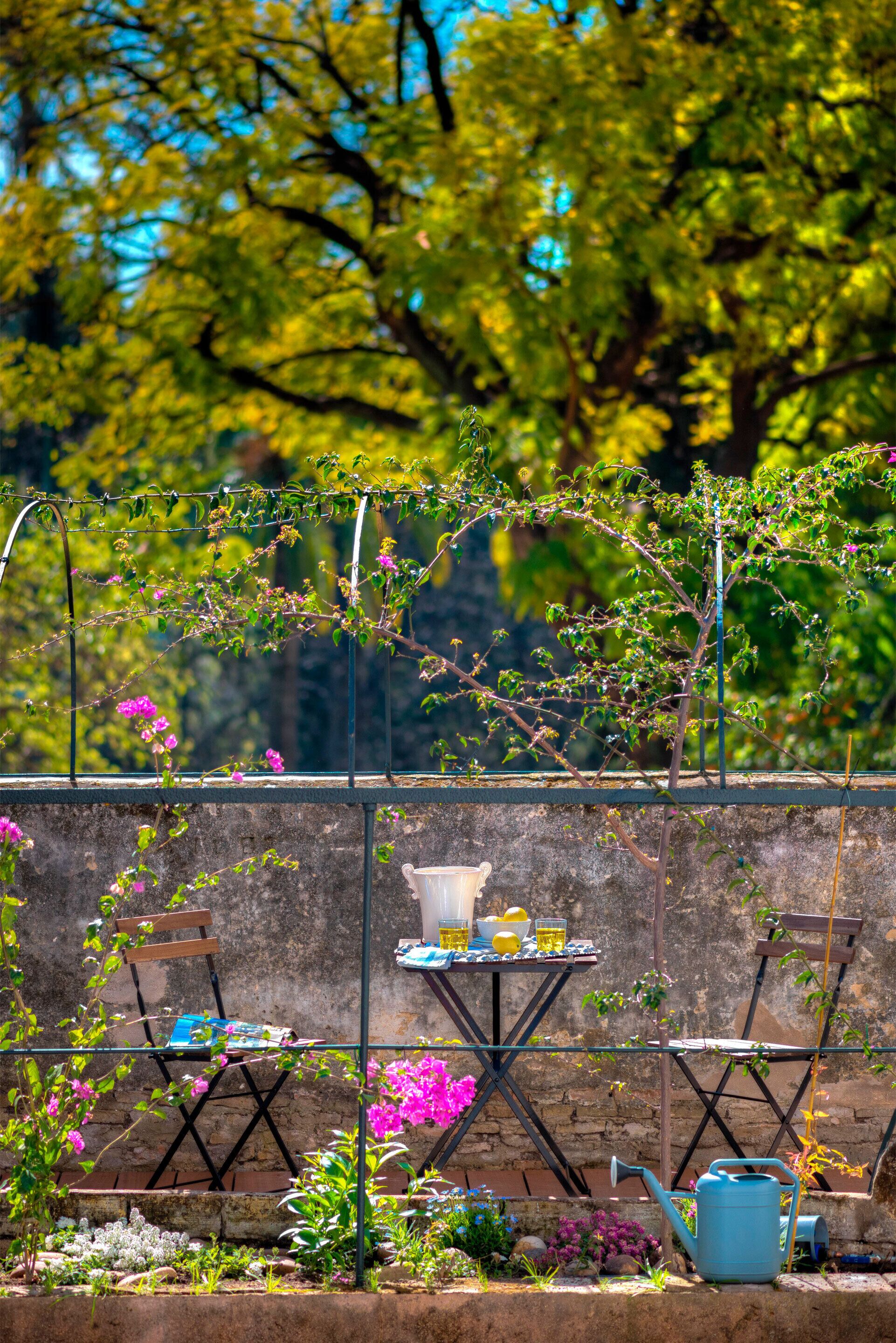 A garden with a table and chairs, a watering can, and a chair with a book.