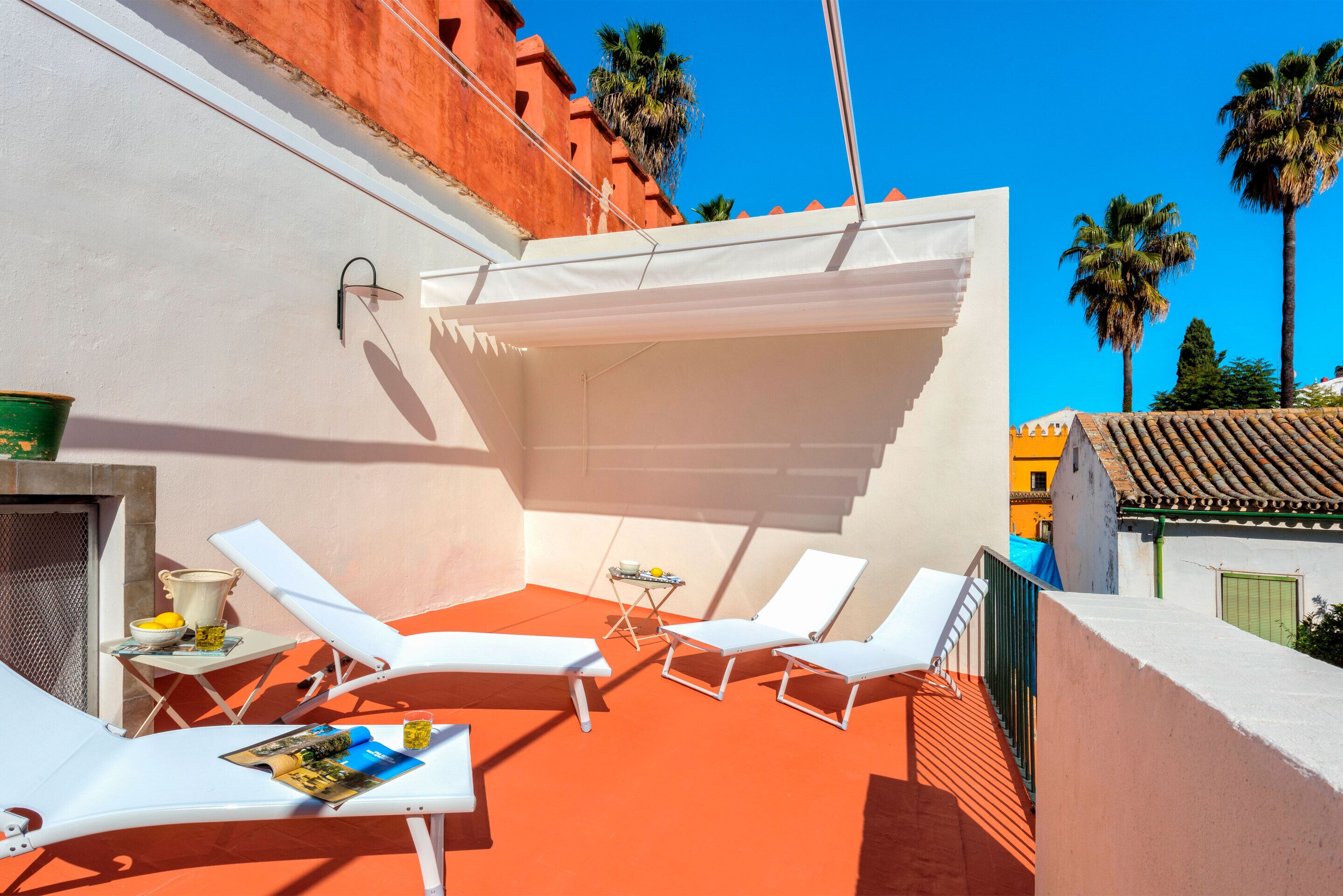 A rooftop terrace with white lounge chairs, a small table with a bowl and a book, and a white awning providing shade.