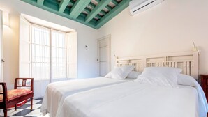 Ein Zimmer mit zwei Betten, einem Sessel, einem Fenster und einer Decke mit sichtbaren Holzbalken.