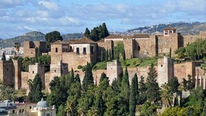 A historic stone fortress with multiple towers and walls, surrounded by greenery and overlooking a cityscape. - Genteel Home Trinidad Grund E (Málaga)