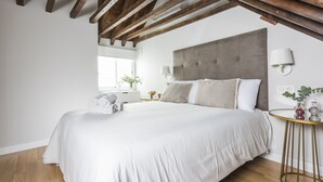 A bedroom with a large bed, wooden beams, a bedside table with a lamp, and a small round table with decorative items. - Genteel Home Trinidad Grund E (Málaga)