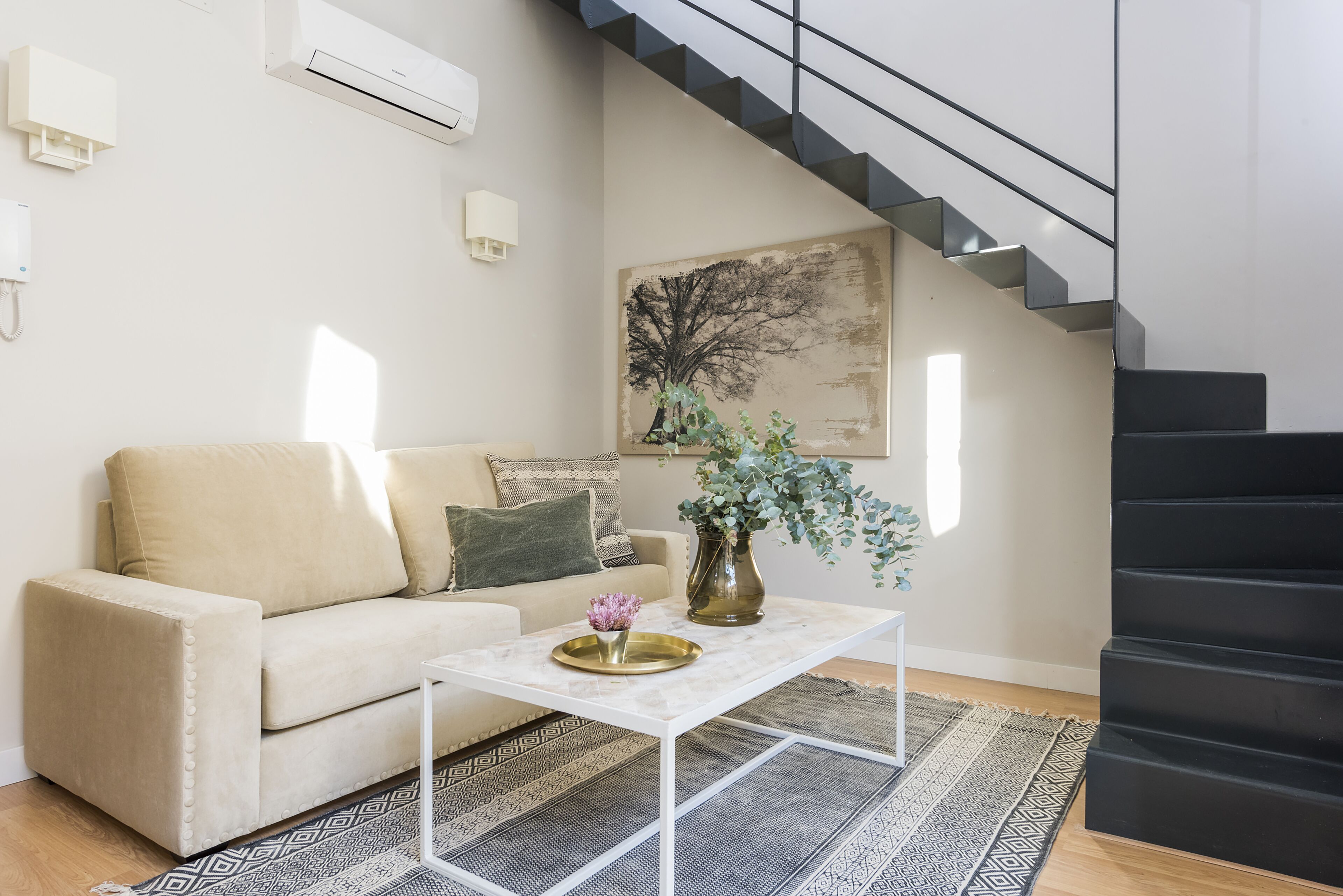 A living room with a sofa, a coffee table, a painting, and a staircase.