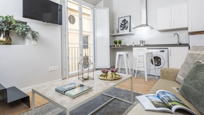 A modern living room with a sofa, a coffee table, a TV, and a kitchen area with a washing machine and a sink. - Genteel Home Trinidad Grund E (Málaga)