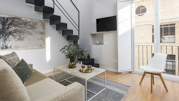 A modern living room with a staircase, a flat-screen TV, a plant, and a white chair. - Genteel Home Trinidad Grund E (Málaga)