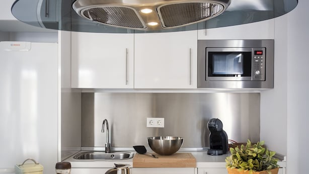 A modern kitchen with a stainless steel range hood, a microwave, a coffee maker, and a wooden cutting board. - Genteel Home Albareda II (Seville)