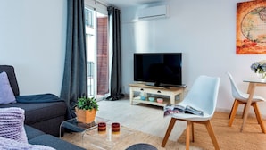 A modern living room with a sofa, a coffee table with a plant, a TV, and a dining area with chairs. - Genteel Home Albareda II (Seville)