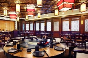 Interior de restaurante tradicional com mesas redondas, cadeiras e lareira central.