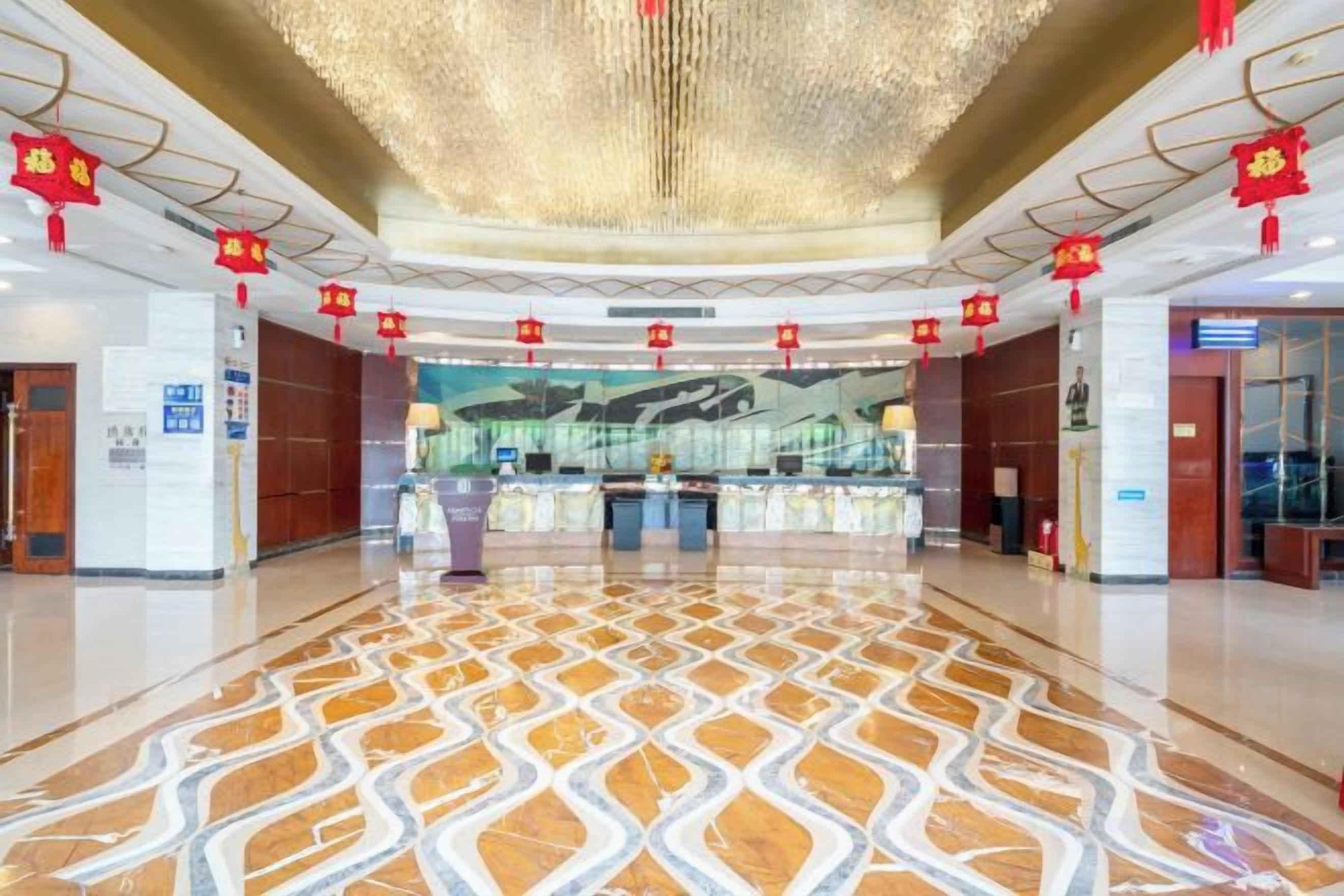 A spacious lobby with a patterned floor, a reception desk, and red decorations.