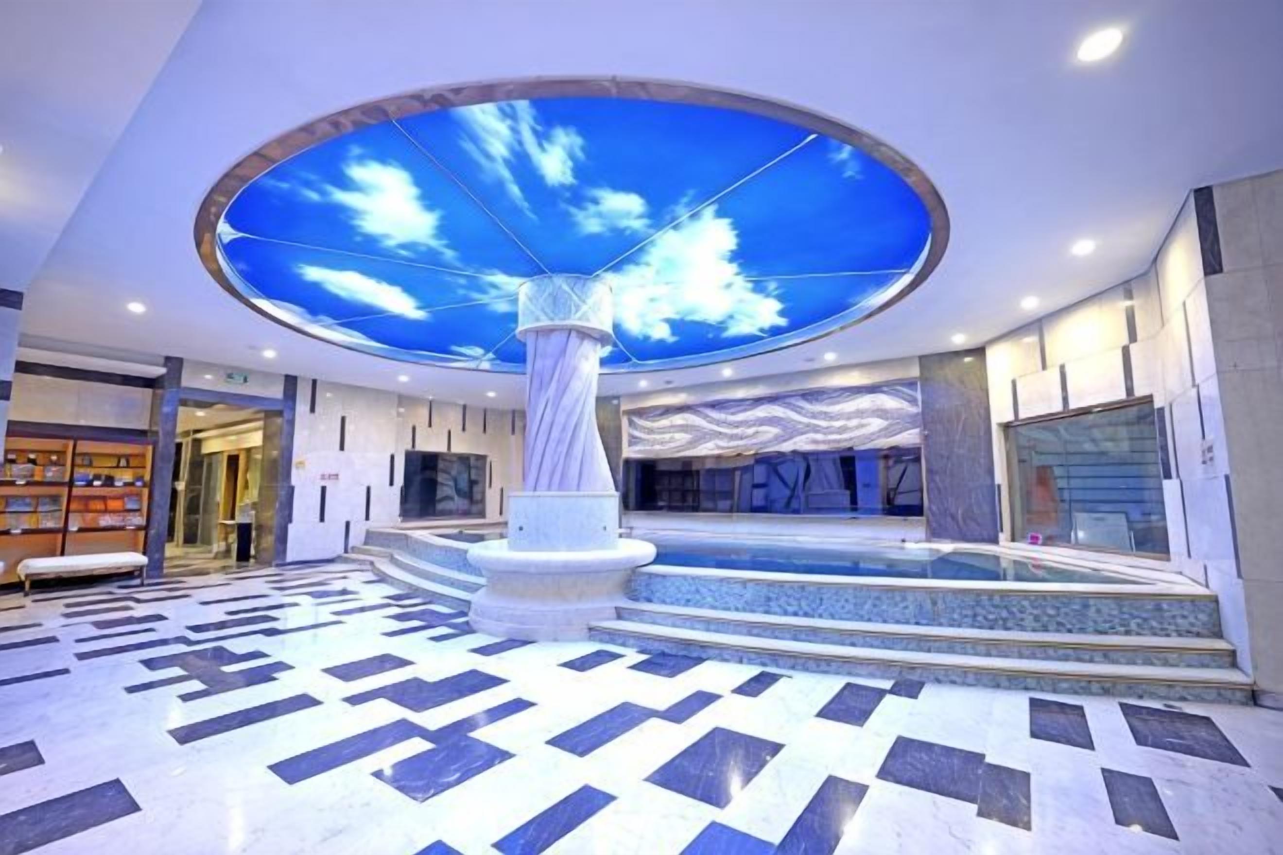 A spacious lobby with a central column, a patterned floor, and a ceiling with a sky-like design.