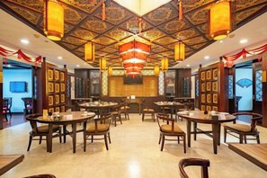 Un restaurante con varias mesas y sillas, techo ornamentado y decoración tradicional.