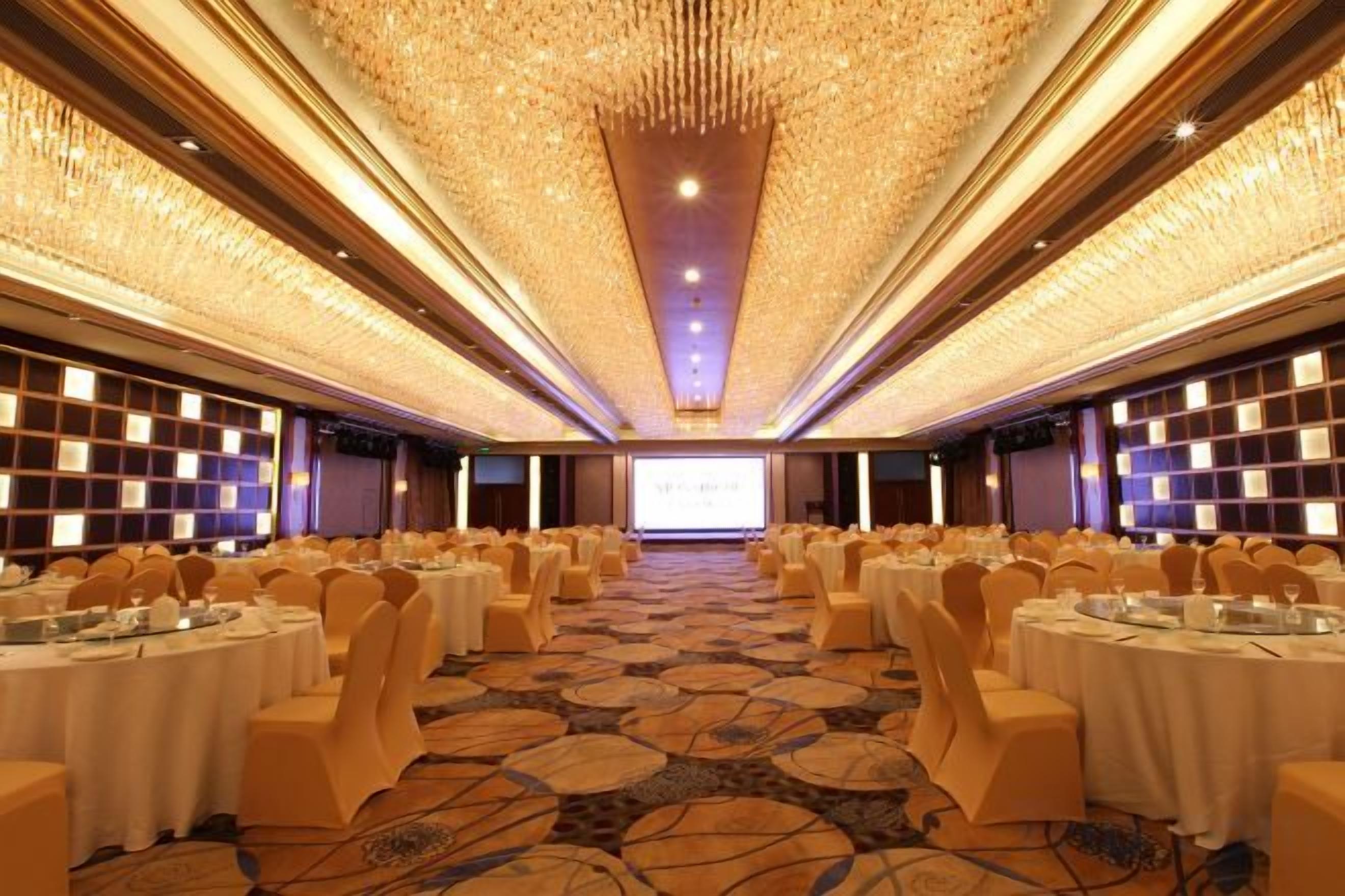 A banquet hall with round tables, chairs, and a projector screen at the front.