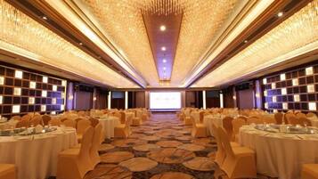 A banquet hall with round tables, chairs, and a projector screen at the front.