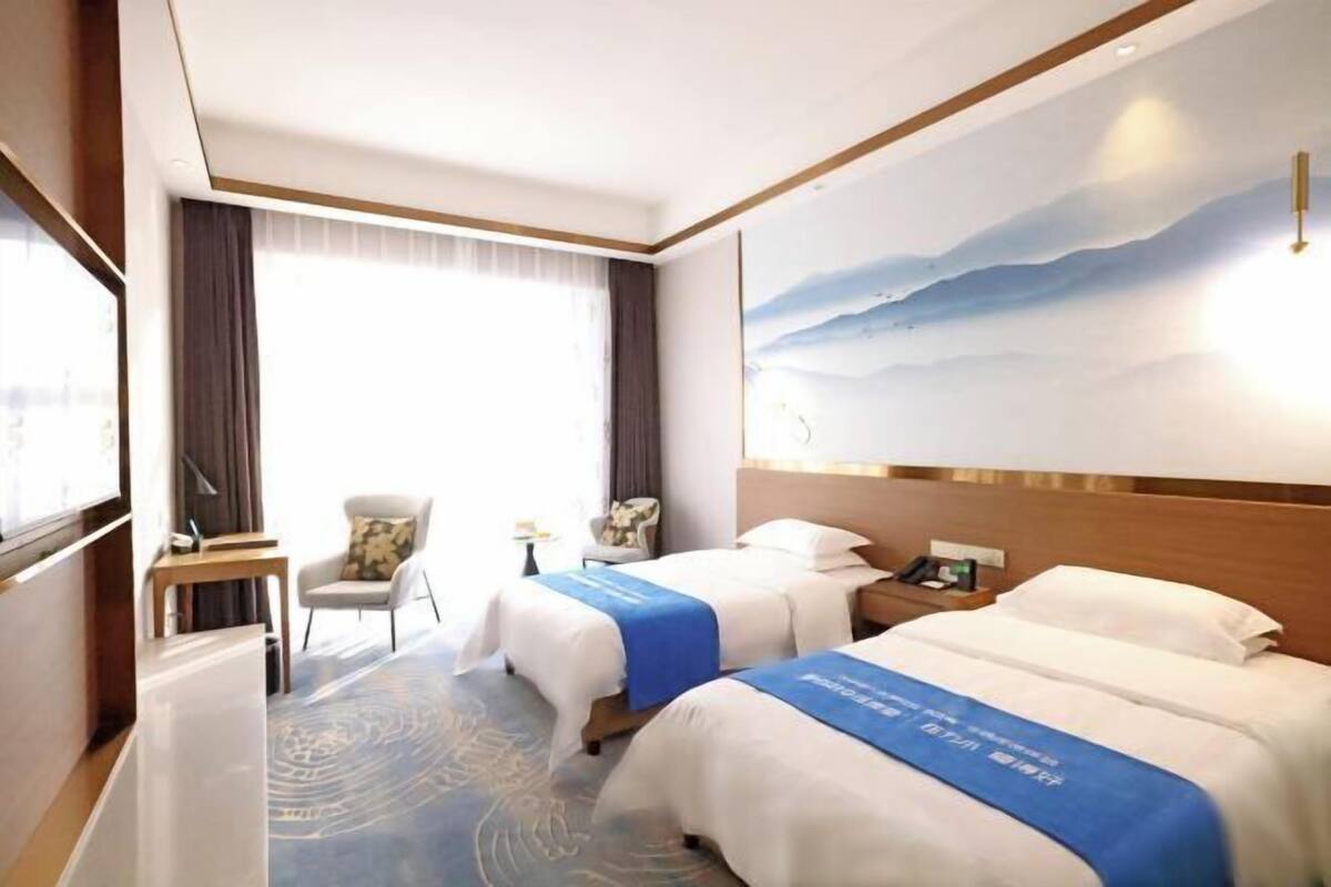 Une chambre d’hôtel avec deux lits, un bureau, une chaise et une grande fenêtre.
