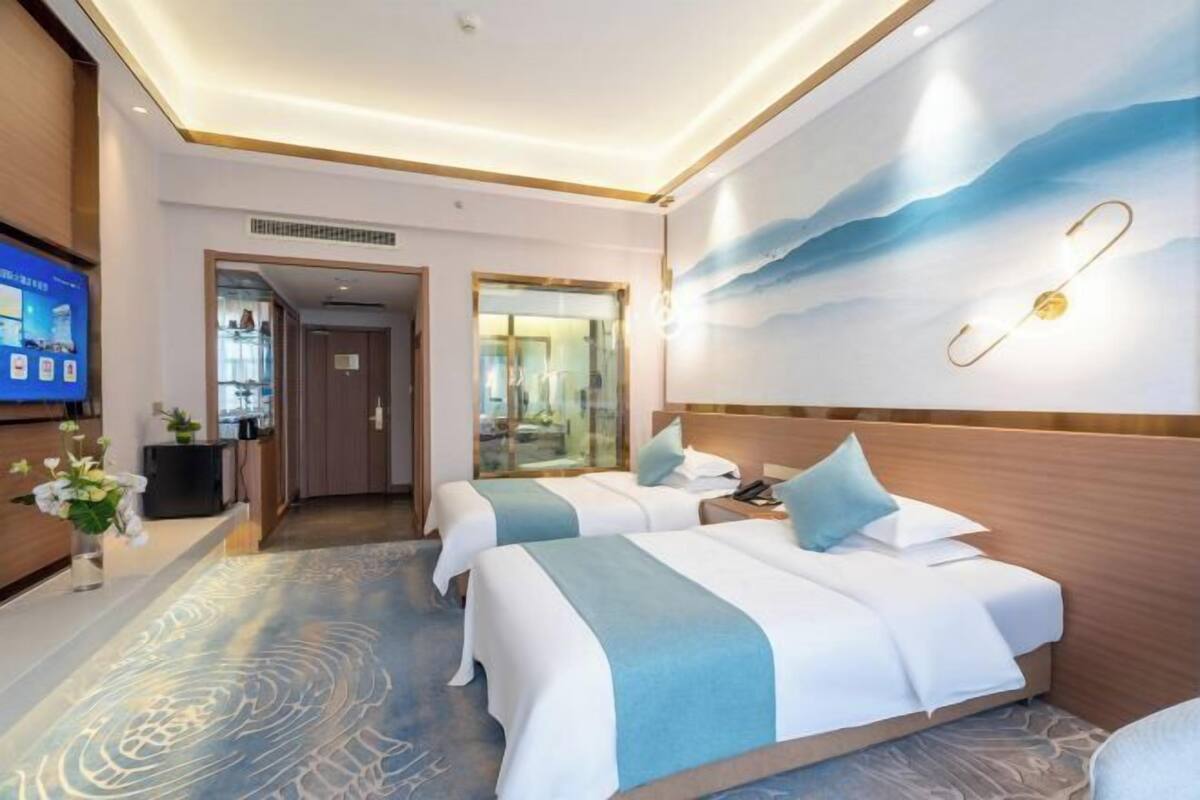 Une chambre d’hôtel avec deux lits, une télévision, un bureau et une salle de bain visible à travers une porte en verre.