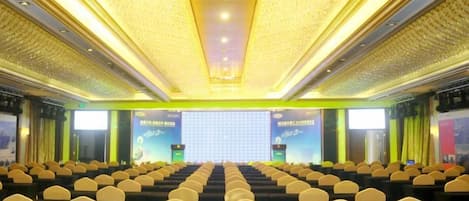 Un salón de conferencias con filas de sillas, un escenario con una pantalla y un techo con diseño.