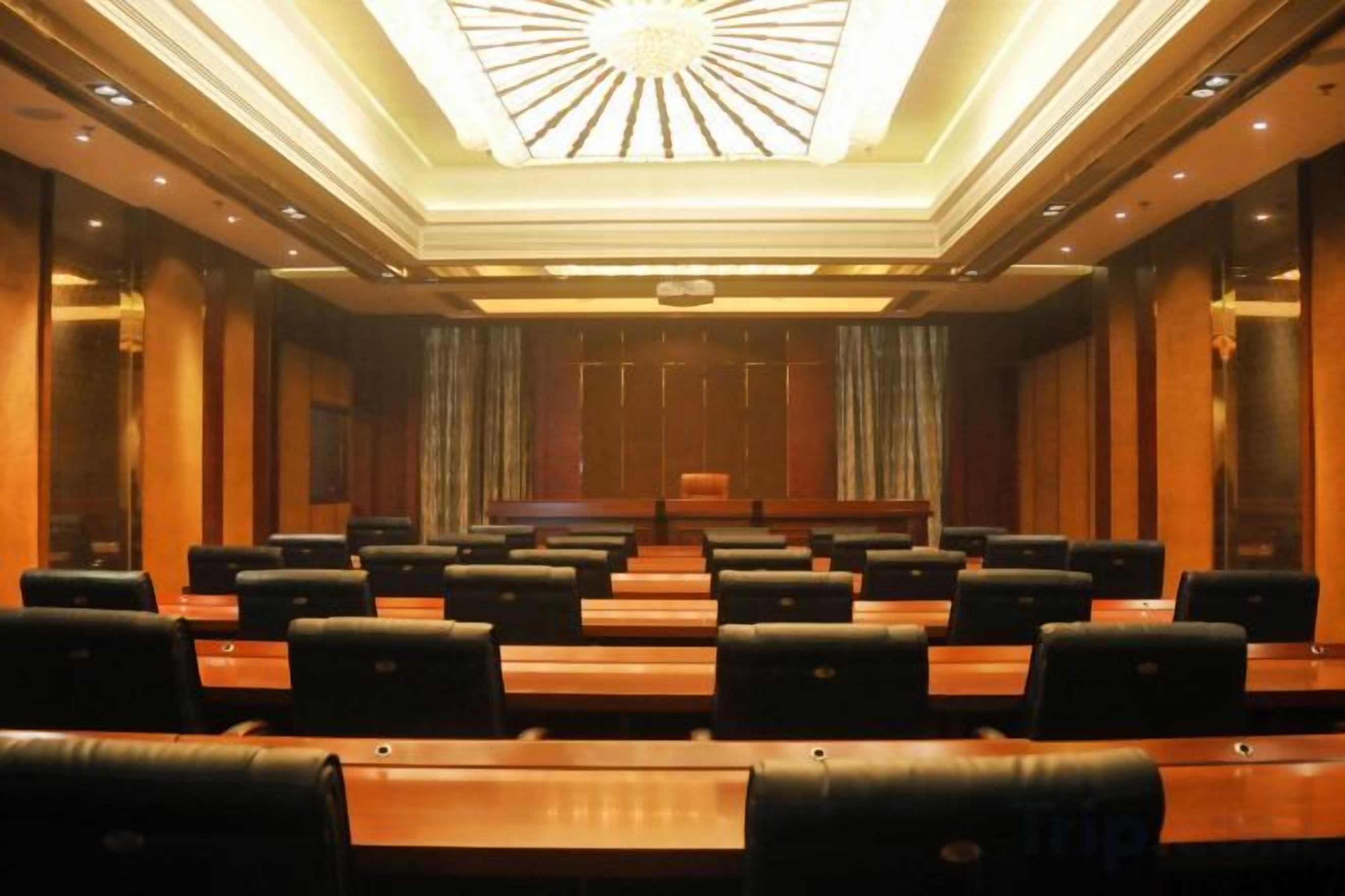 A conference room with rows of tables and chairs, a podium, and a large chandelier.