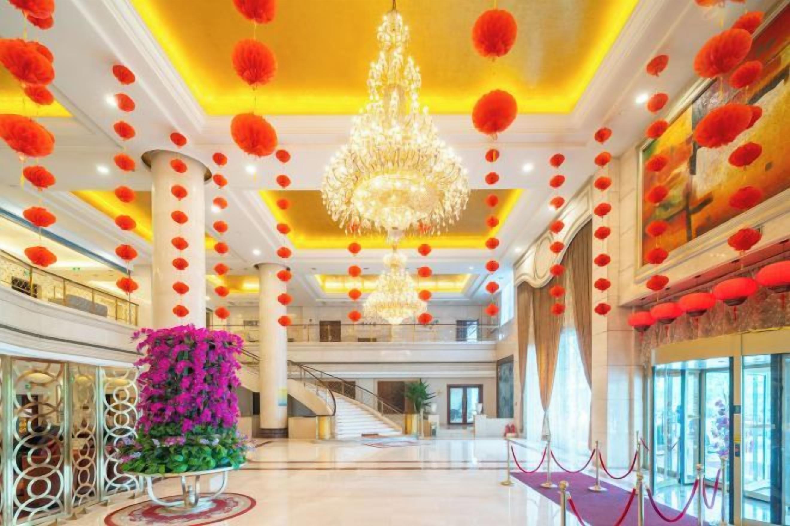 A spacious lobby with a grand chandelier, red lanterns, and a staircase leading to upper floors.