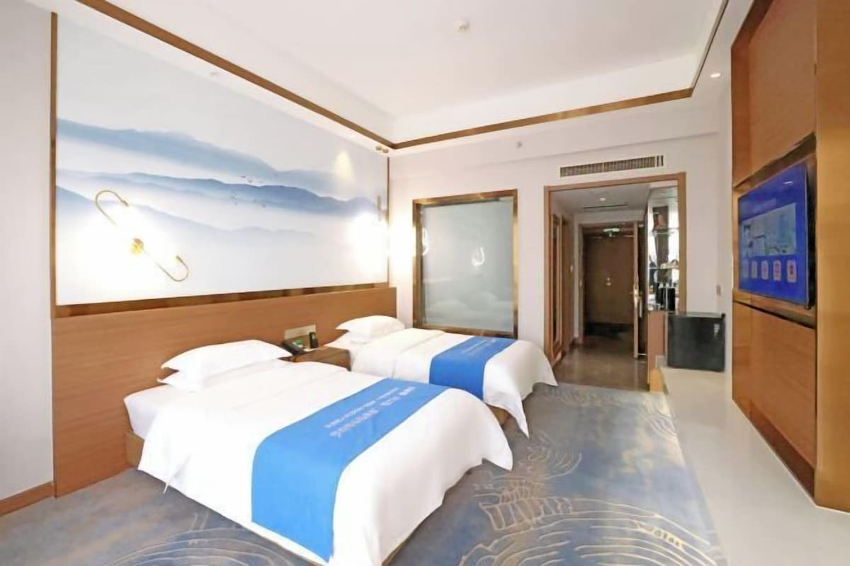 Une chambre d’hôtel avec deux lits, une grande fresque murale et un téléviseur.