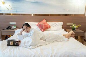 Una habitación de hotel con una cama, una mesita de noche con lámpara y un atril con teléfono.