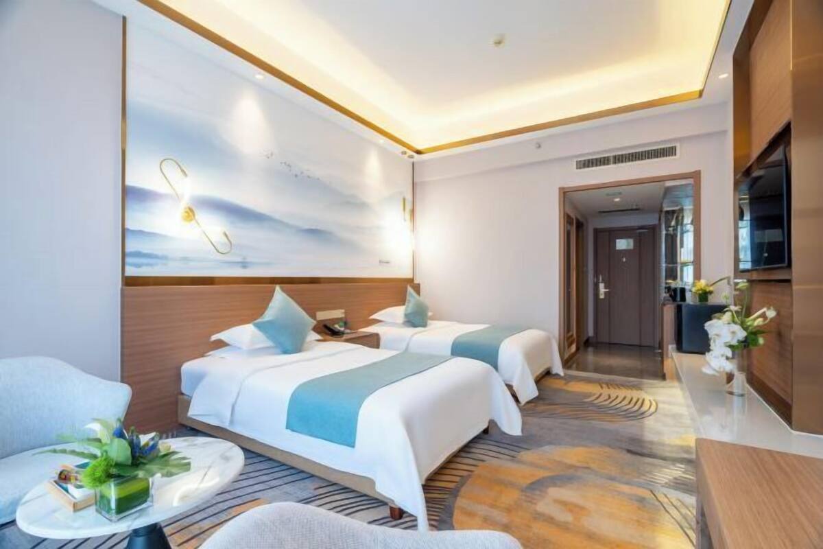 Une chambre d’hôtel avec deux lits, un coin salon avec une table et des chaises, une télévision et un comptoir de réception.