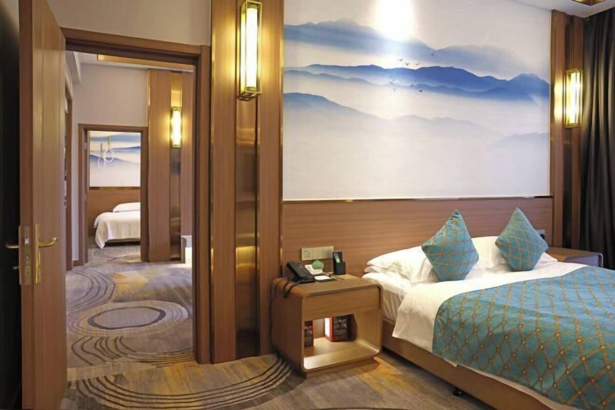 Une chambre d’hôtel comprenant un lit, une table de chevet, une commode et un mur orné d’un tableau représentant un paysage de montagne.