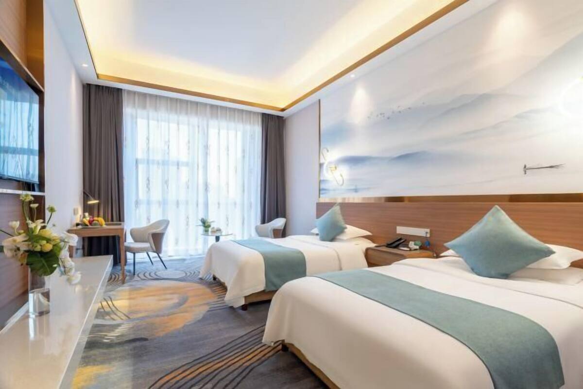 Une chambre d’hôtel avec deux lits, un bureau, une chaise et une grande fenêtre avec des rideaux.
