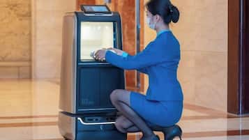 A woman in a blue dress using a self-service kiosk in a lobby with marble flooring and a glass door in the background.