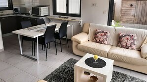 A modern kitchen with a dining area, a sofa, and a small side table with a decorative item. - TI BIHAN housing >> (Bénodet,)