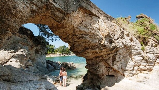 A natural rock formation with a clear archway, a sandy beach, and calm water. - TI BIHAN housing >> (Bénodet,)