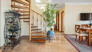A wooden staircase with a metal wine rack on the left, a large potted plant in the center, and a dining area with chairs and a table on the right. - *****Fewo Mariposa - luxury beach penthouse 200sqm, great sea view, free garage (Guardamar)