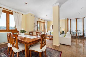A spacious living area with a dining table, chairs, a sofa, and a balcony.