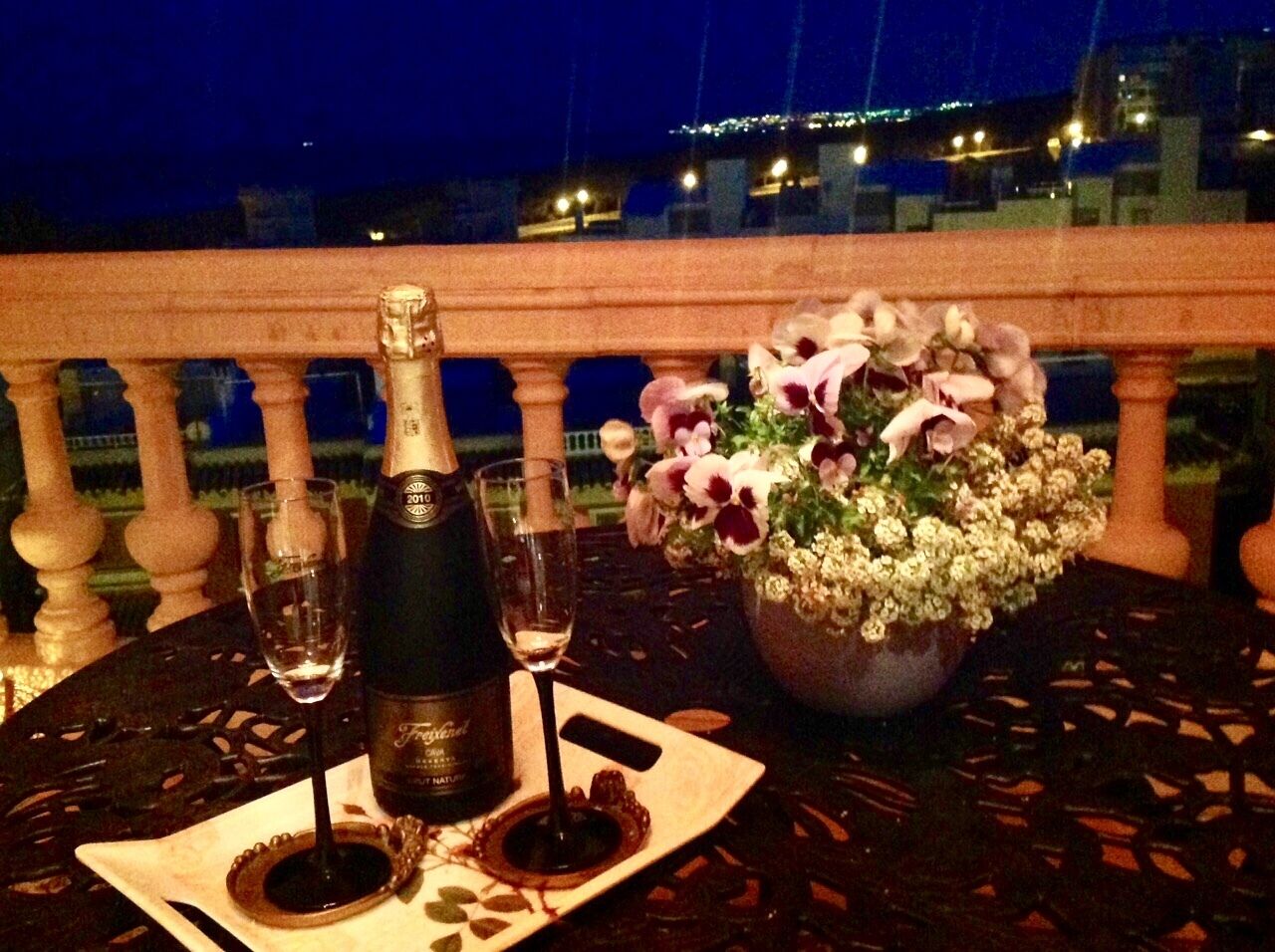 A table with a bottle of champagne, two glasses, and a floral arrangement.