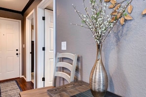 Un coin repas avec une table, des chaises, un vase décoré de branches et une porte en arrière-plan.