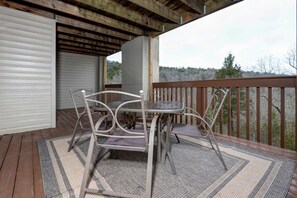 A covered outdoor area with a table and chairs, a wooden deck, and a view of trees.