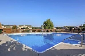 Une piscine avec un escalier en métal, entourée de maisons, sous un ciel d’un bleu éclatant.