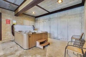 A hot tub in a room with a concrete wall and a wooden bench.