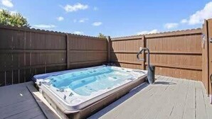 Een hottub op een houten terras, met een houten omheining op de achtergrond.