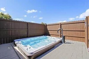 Un bain à remous sur une terrasse en bois, avec une clôture en bois en arrière-plan.