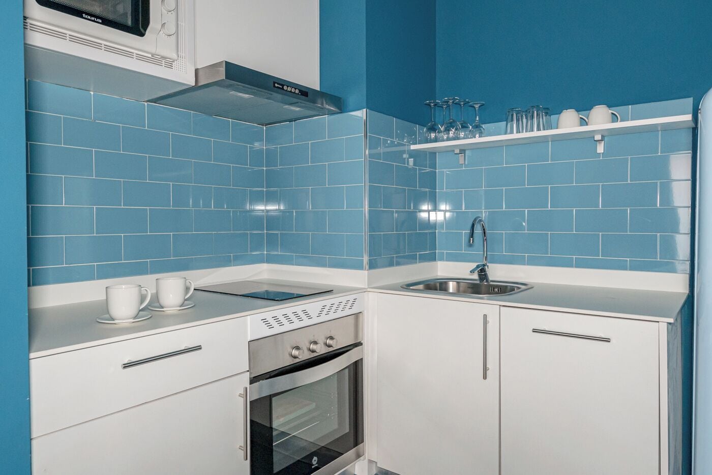 A compact kitchen with blue tiles, a built-in oven, a microwave, and a sink.