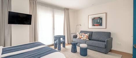A modern hotel room with a bed, a sofa, a TV, and a window with curtains.